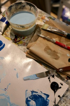 Paint brushes, rinsing bowl and scraper all covered with various colors of paint